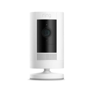 De RING Stick Up Cam Batterij - Beveiligingscamera is een witte beveiligingscamera met een zwart voorpaneel, centrale lens en luidsprekerrooster aan de onderkant op een ronde basis, afgebeeld tegen een effen witte achtergrond.
