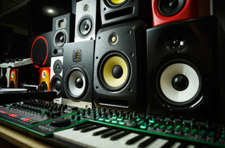 Een close-up van een muziekstudio met meerdere studiomonitorluidsprekers en een synthesizerklavier met oplichtende groene lampjes.