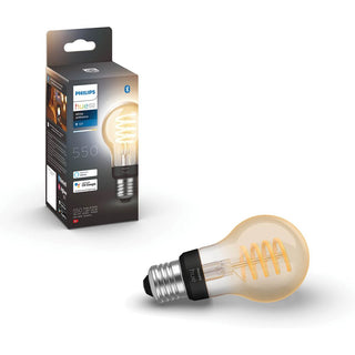 Een Philips Hue filament standaardlamp A60 van Philips wordt getoond naast de verpakking, waarop de afbeelding van de lamp te zien is. De slanke verlichting geeft een warme gloed en de doos benadrukt de ondersteuning voor Bluetooth en smart home assistent.