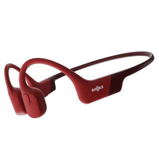 De SHOKZ OpenRun in rood is een open hoofdtelefoon met beengeleiding en draadloze omsluitende hoofdband, getoond op een witte achtergrond. Het SHOKZ-logo staat zichtbaar op één oorkussen.