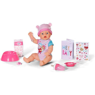 Een Baby Born Emma - Babypop 43 cm van Baby Born, gekleed in een roze hoed en onesie, wordt geleverd met een magisch bord, kom, lepel, fopspeen, fles, luier, wenskaart en stickervel.