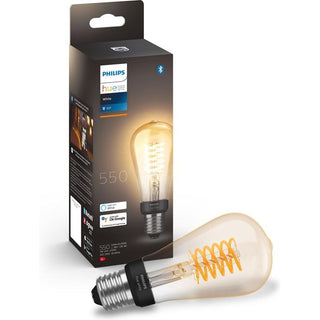 Een Philips Hue Filament Lichtbron E27 ST64 Edison LED-lamp van Philips, vormgegeven als een vintage Edison lamp, wordt voor de doos geplaatst waarop de lamp te zien is en voorzien is van Bluetooth en slimme verlichting stemassistent compatibiliteit.