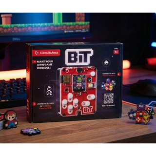 Een DealFixers Retro Gaming Handheld (Zelfbouw / Bouwpakket) doos staat op een bureau met pixel art, toetsenbord en monitor waarop retro games te zien zijn. De box benadrukt functies zoals videogames maken en programmeren in MicroPython.