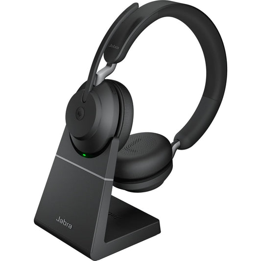 Een paar zwarte Jabra Evolve2 65 MS Stereo Bluetooth headphones rust op de meegeleverde oplaadstandaard, die een groen indicatielampje en het Jabra-logo weergeeft - ideaal voor Microsoft Teams-gesprekken.