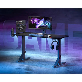 Het DealFixers Pro-Series Gamingbureau met RGB LED Verlichting en PEG Board heeft een heavy-duty opstelling met een grote monitor, mechanisch toetsenbord, muis, RGB-accenten, koptelefoonhouder, bekerhouder en pegboard-accessoires tegen een paarsblauwe achtergrond.