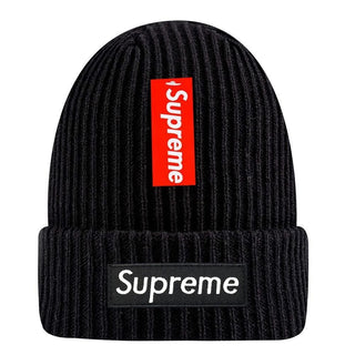 De Supreme New Era® Box Logo Beanie - Zwart is een zwarte gebreide muts met een rood verticaal Supreme label en een zwarte horizontale Supreme patch op de vouw, waardoor stijl en exclusiviteit samenkomen in dit limited edition accessoire.